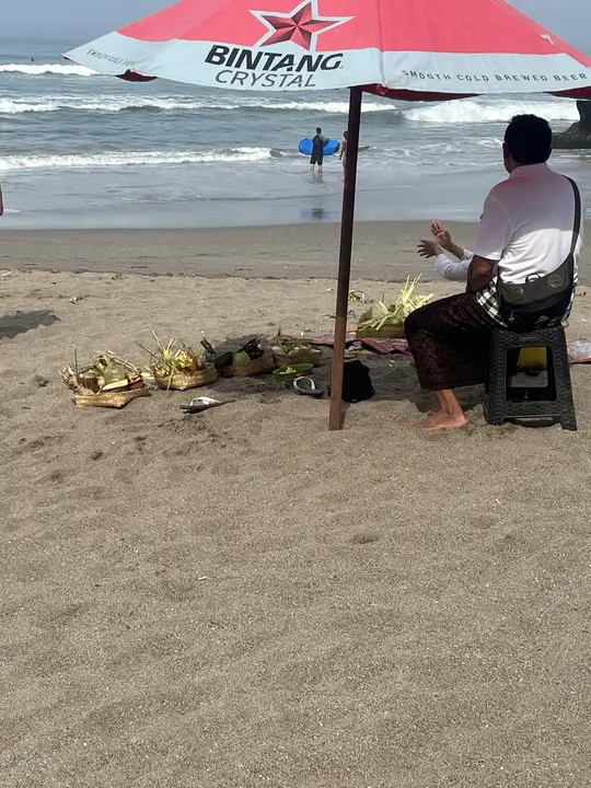 A man praying in front of a row of offerings on the beach.