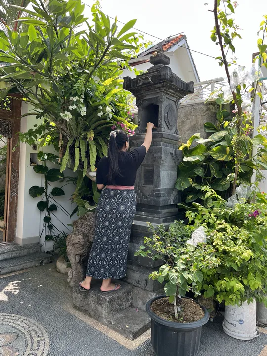 Placing an offering inside the stone shrine in front of the house.